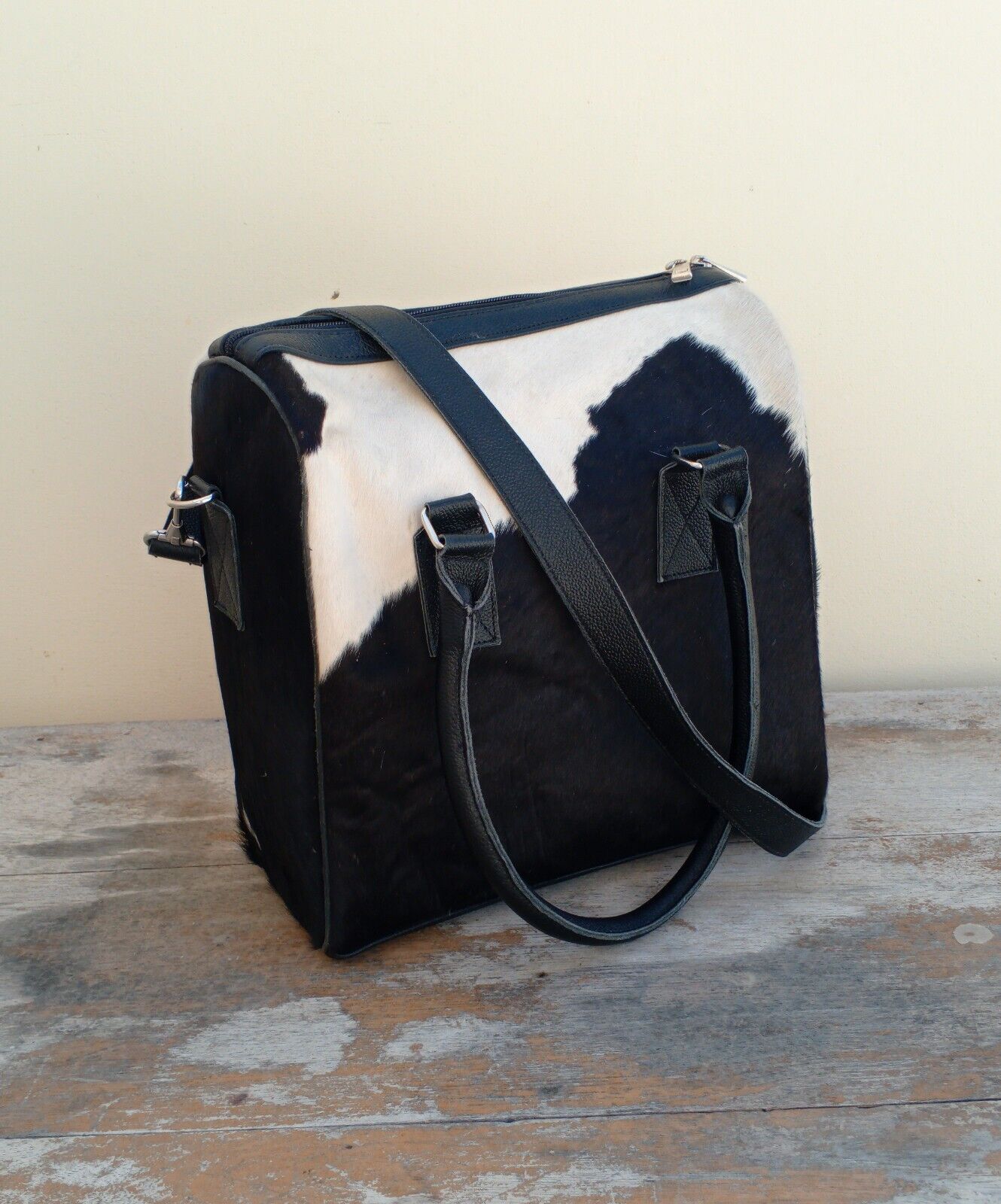 Cowhide handbag placed beside coffee and sunglasses on an outdoor table.