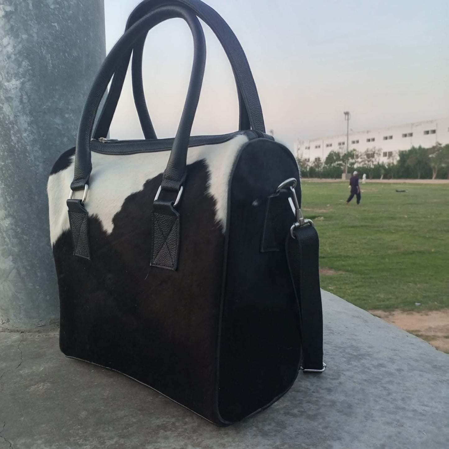 Elegant bridesmaid holding a cowhide shoulder bag at a rustic wedding.