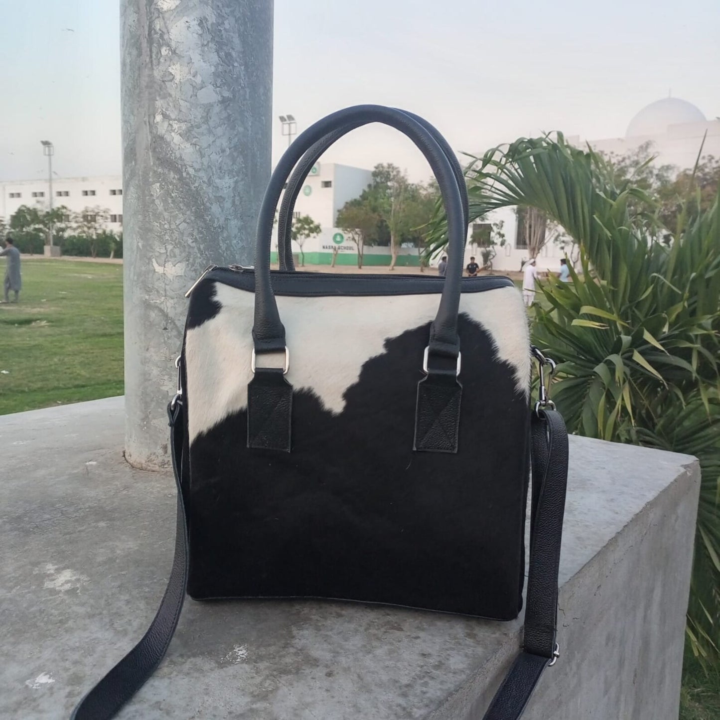 Handcrafted cowhide shoulder bag with intricate patterns on a wooden table.