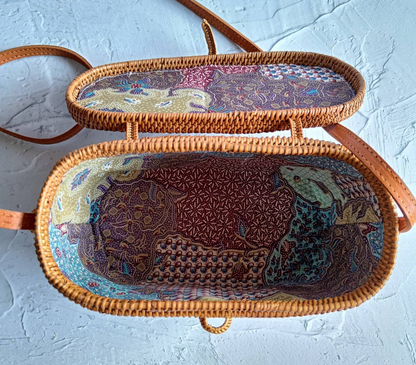 Artisan weaving an oval rattan crossbody bag in a lush forest setting.