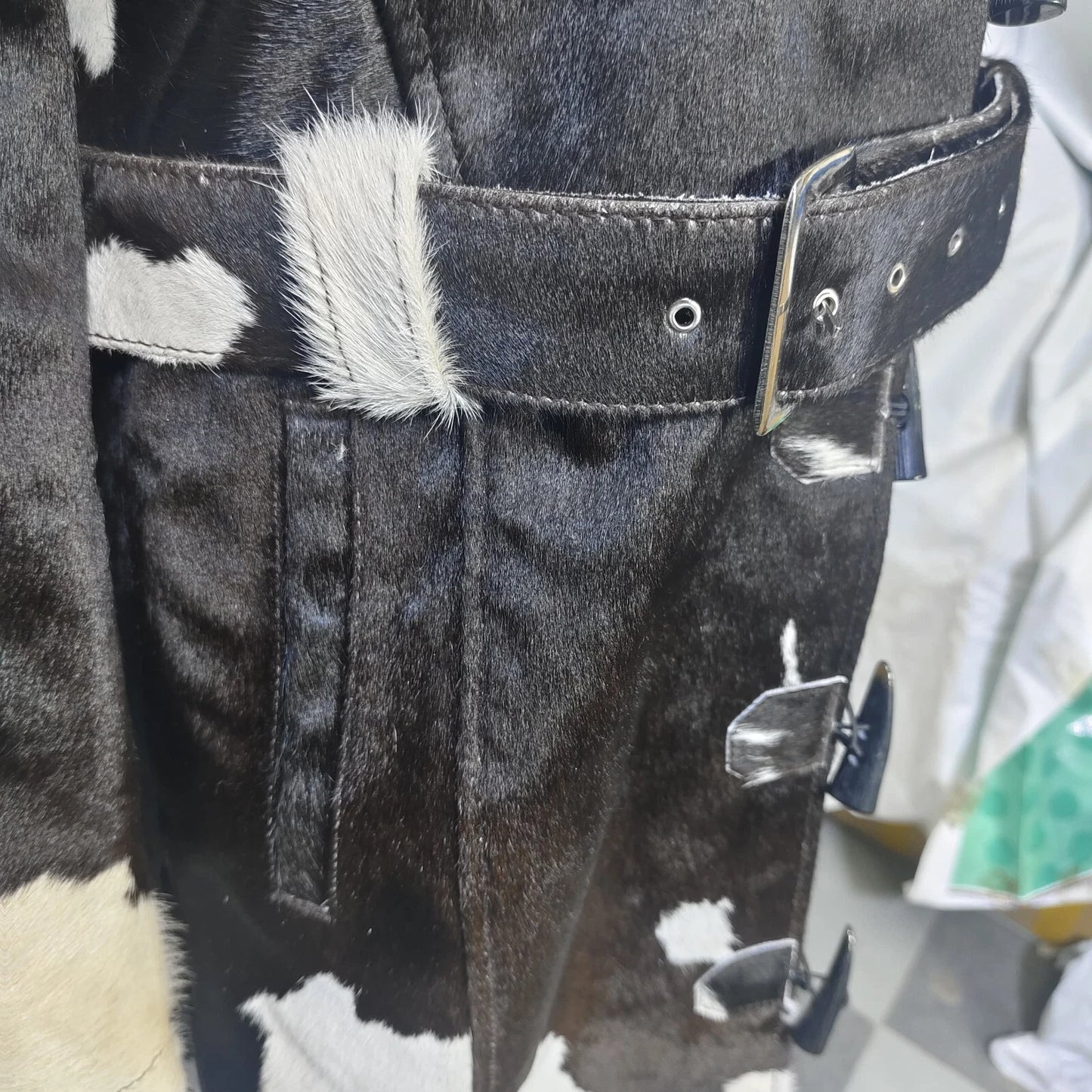 Get noticed in a genuine leather cowhide trench coat with horn toggles, a belted waist, and natural cow print design—each coat is one of a kind.