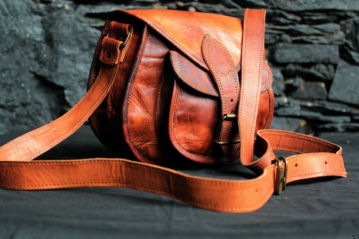 Elegant tan leather messenger bag for men, perfect for work or travel, placed on a wooden table with essentials spilling out.
