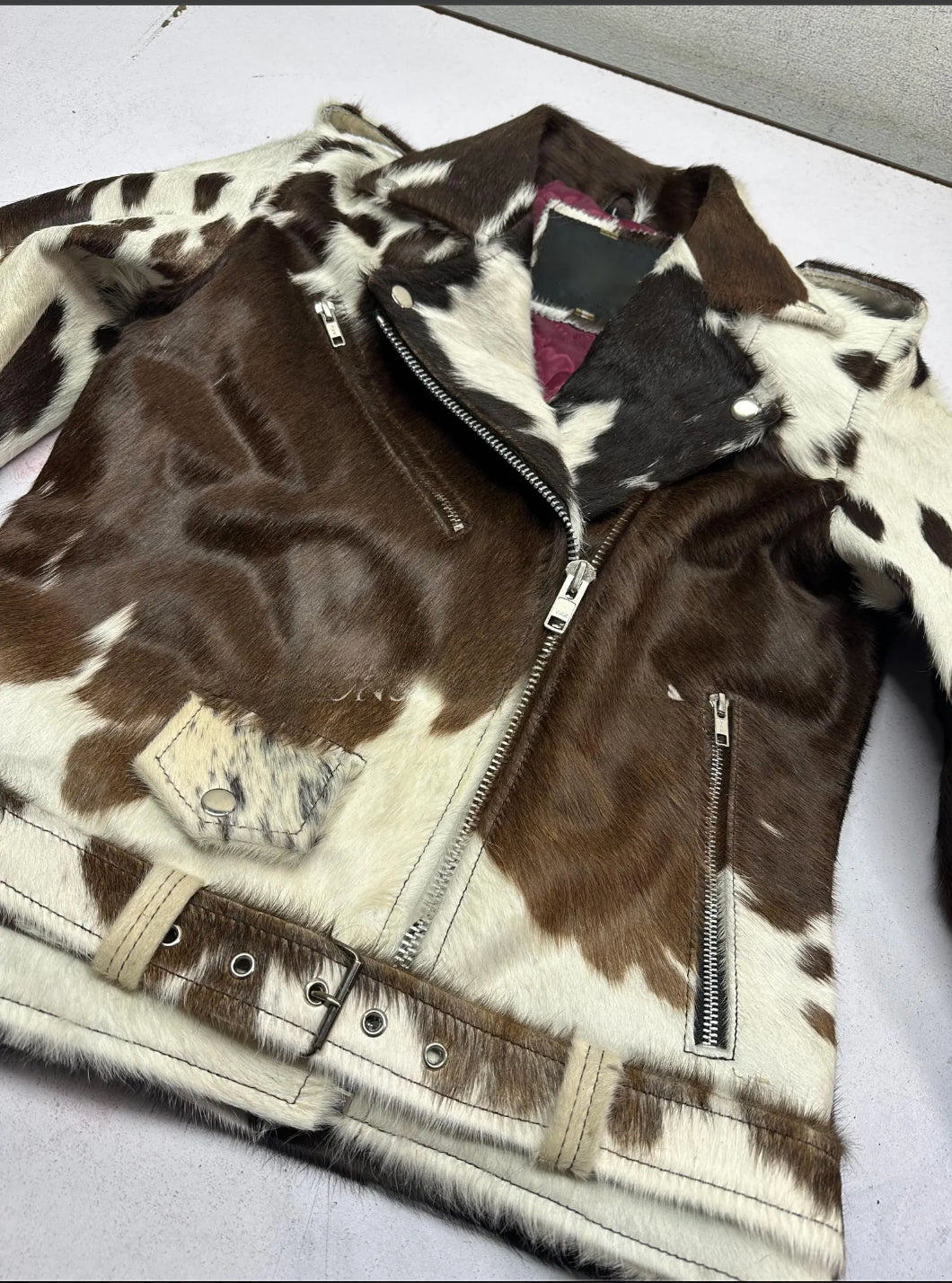 Real hair-on cowhide leather jacket for men featuring black, brown, and white patches, asymmetrical front zipper, and classic biker fit. Shop genuine cowhide coats.