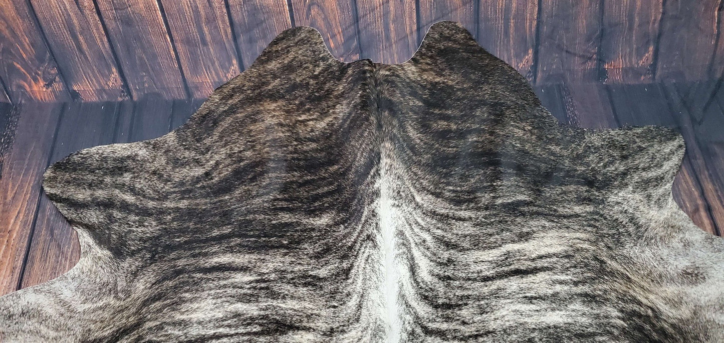 A luxurious grey brindle cowhide rug, sourced from Brazil, displayed on a hardwood floor. The natural patterns and hues of grey are prominently visible, enhancing the sophisticated aesthetic of the room.