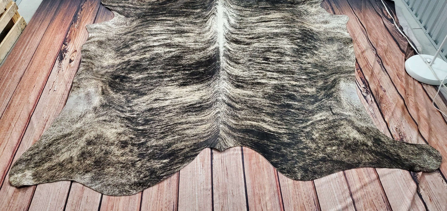 The cowhide rugs are a statement piece and free shipping all over the USA.A room setting showcasing a large grey brindle cowhide rug under a wooden coffee table. The rug's muted colors and striking pattern complement the modern decor of the living space