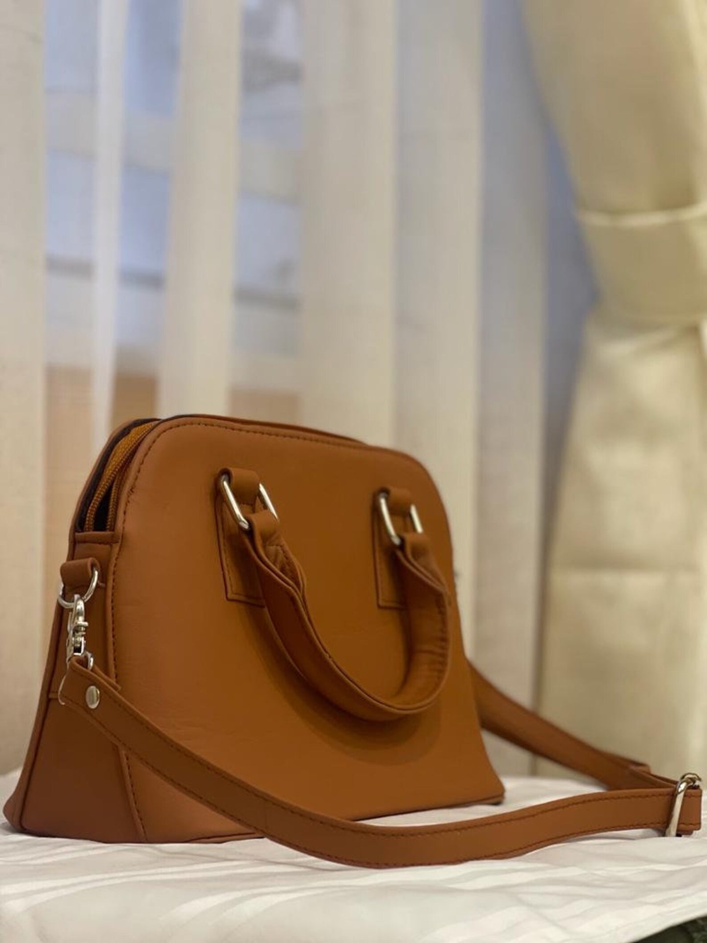 Tan leather crossbody bag with a front pocket and zipper detail, hanging from a wooden coat rack.