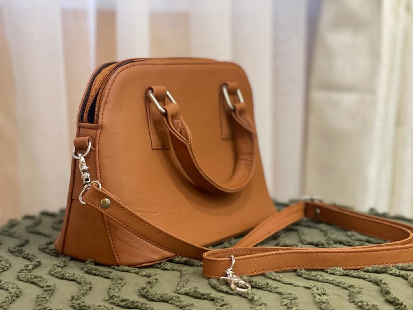 A chic leather crossbody bag with a gold chain strap, placed on a marble countertop.