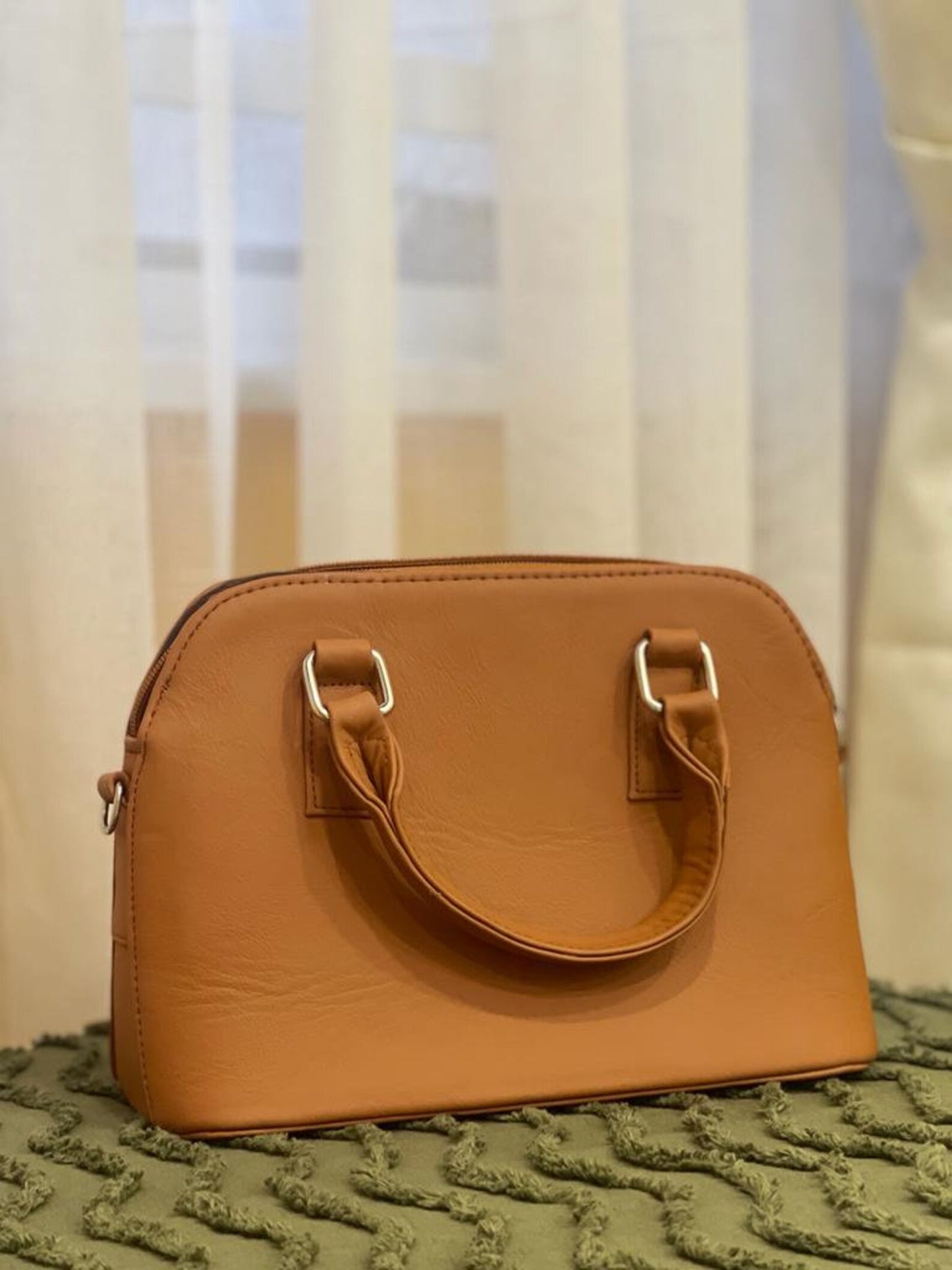 Small, sleek leather crossbody bag in deep brown, displayed on a cozy knit blanket.