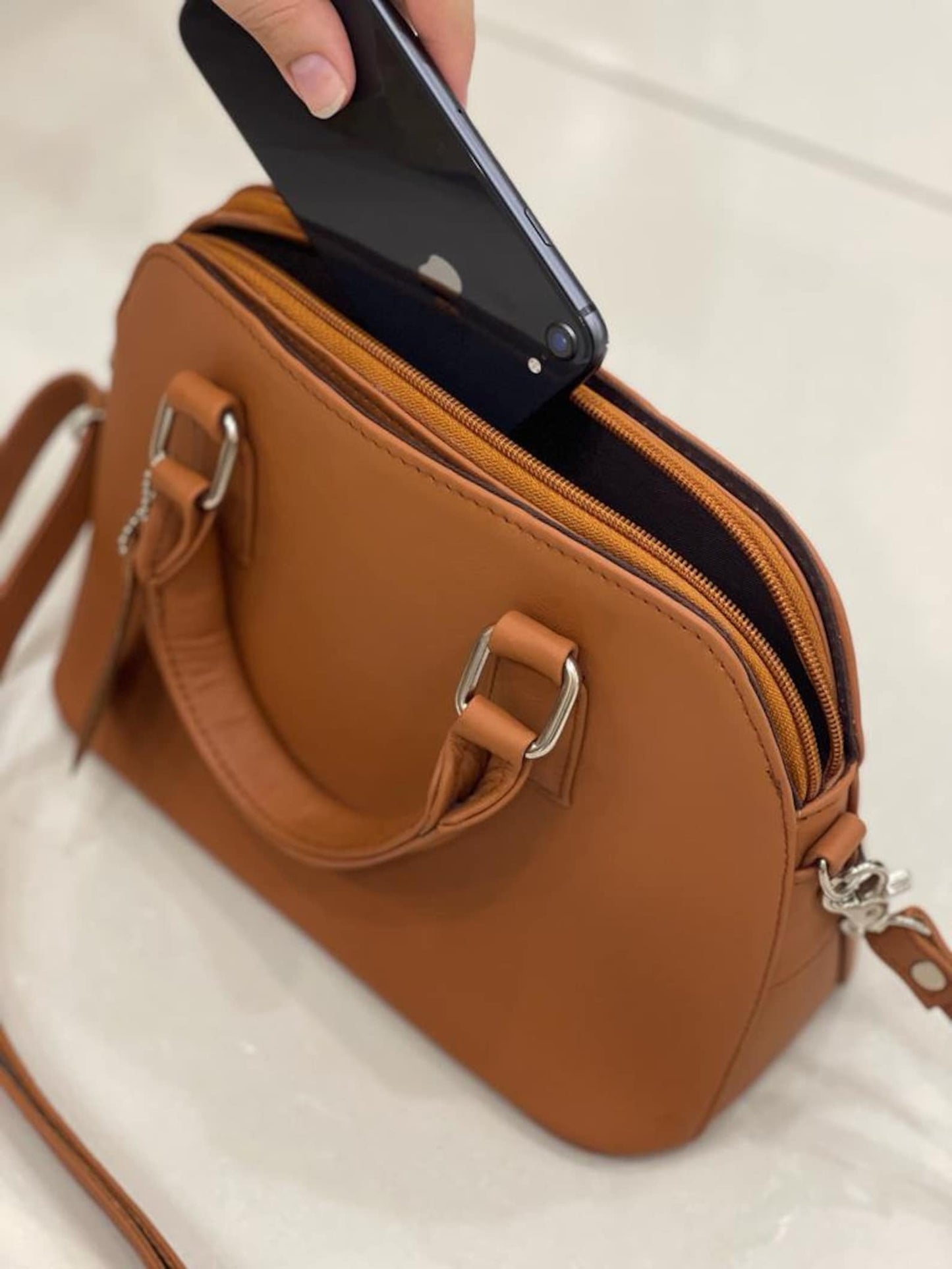 A modern leather crossbody bag with adjustable strap, resting on a sunlit windowsill.