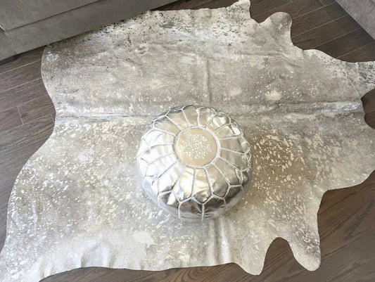 metallic cowhide rug and leather poufs hand in hand.