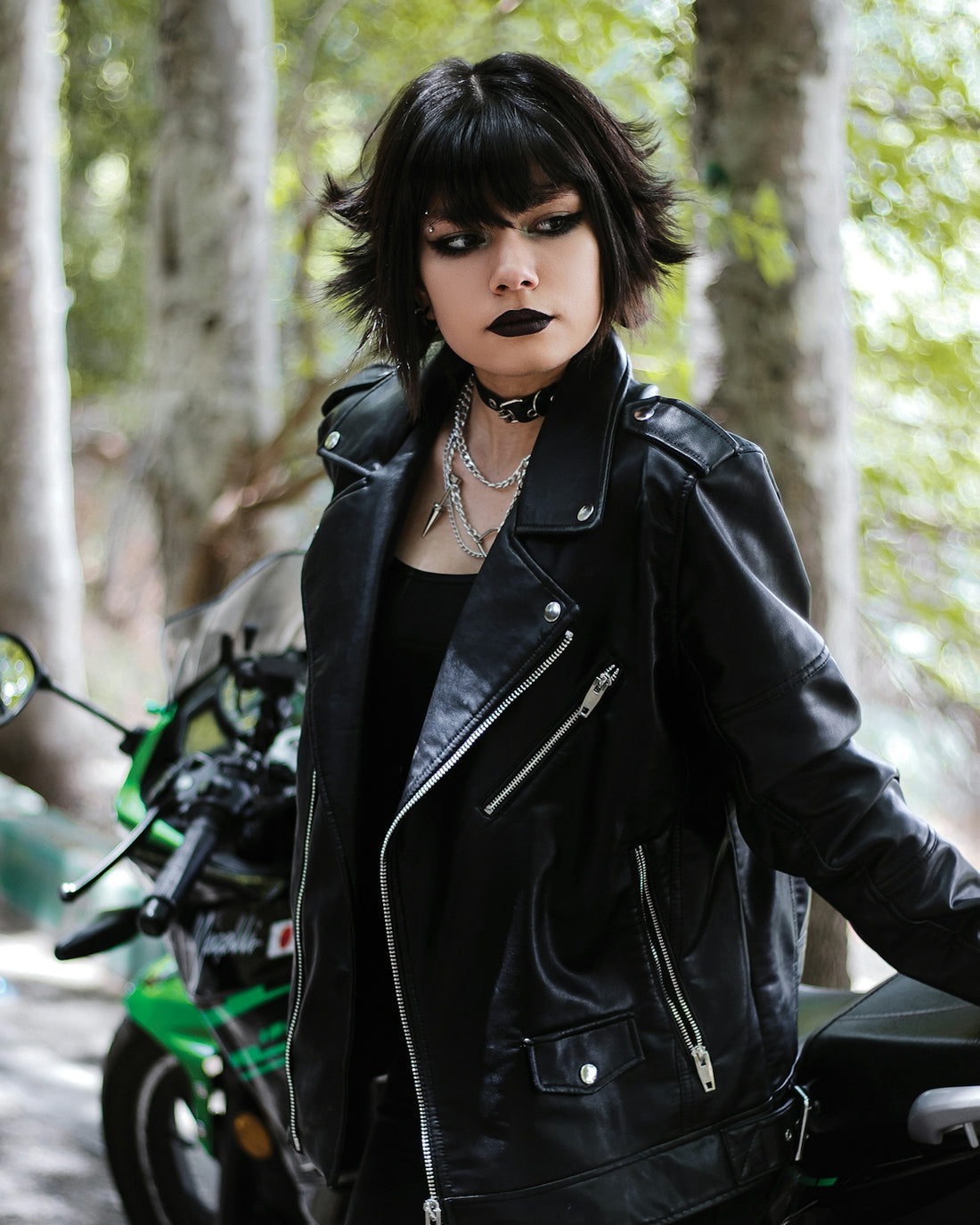 a woman in a black leather jacket standing next to a motorcycle