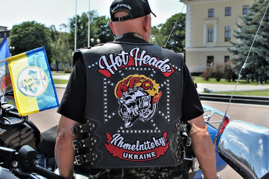 A man in a leather vest standing next to a motorcycle