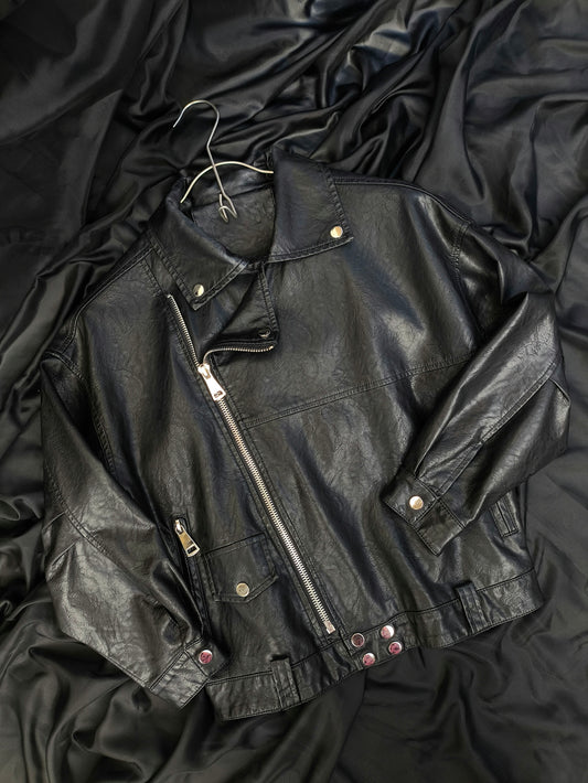 A black leather jacket laying on top of a bed