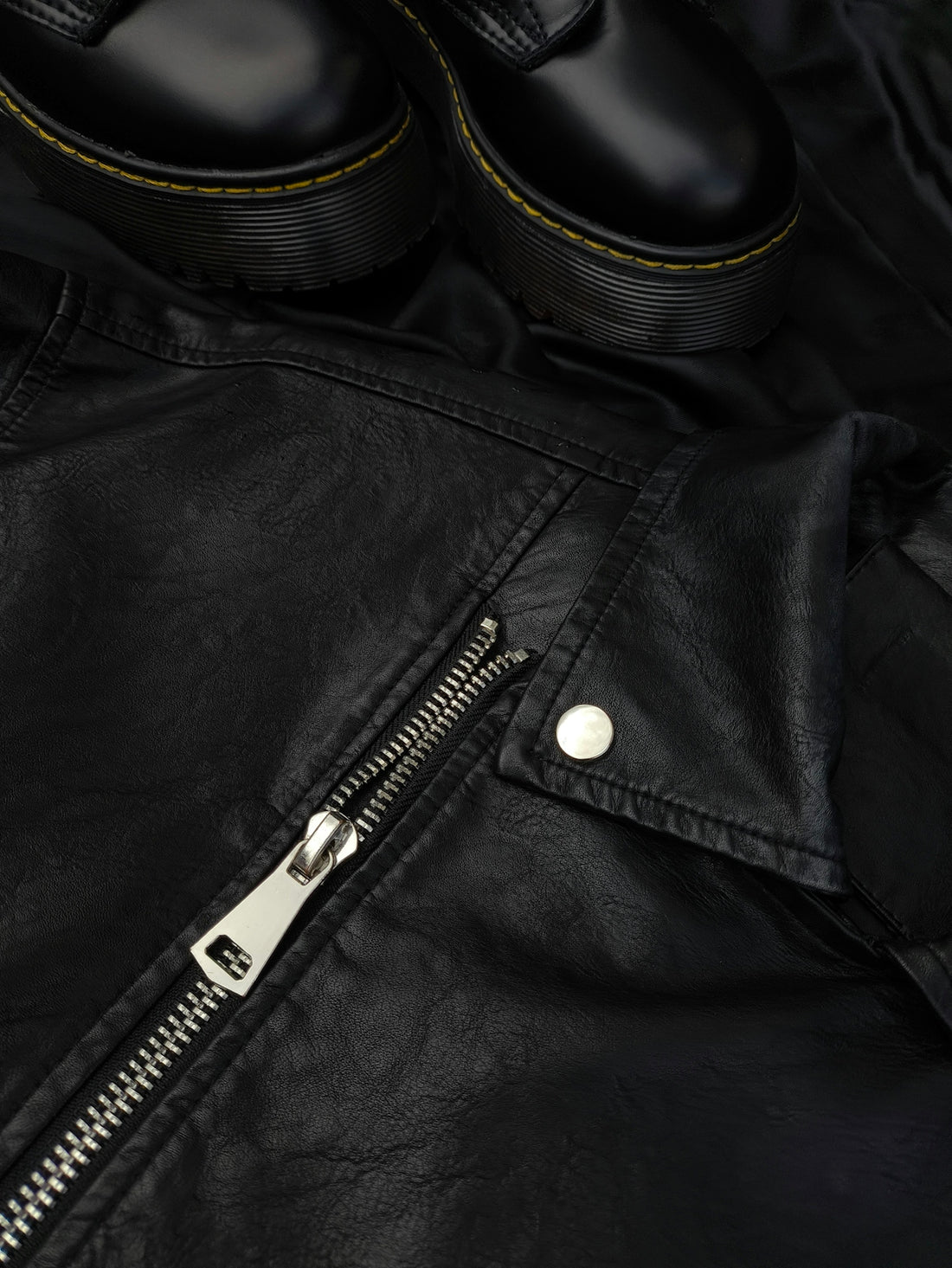 A pair of black shoes sitting on top of a black leather jacket