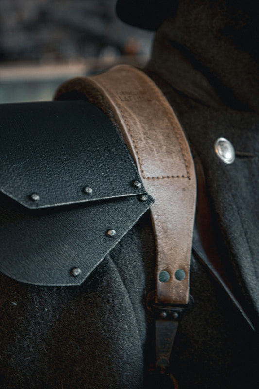 A man wearing a black jacket with a brown leather bag on his back