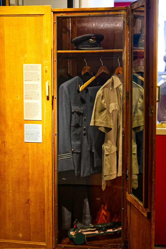 An open wardrobe displays military uniforms and accessories.