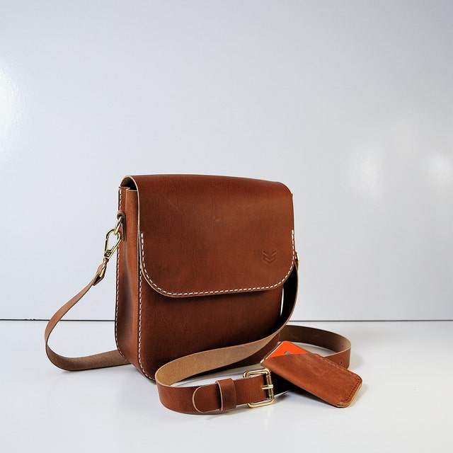 A leather messenger bag displayed against a rustic wooden background. The bag features multiple compartments, adjustable straps, and metallic hardware. Its rich texture and classic design exude sophistication and timeless style