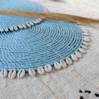 Set of dyed blue seagrass round placemats with cowrie shells