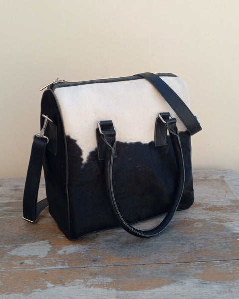 A stylish cowhide handbag on a wooden table, complementing casual clothes.