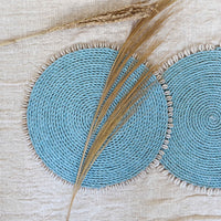 Set of dyed blue seagrass round placemats with cowrie shells