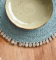 Set of dyed blue seagrass round placemats with cowrie shells