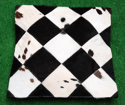 Black white cowhide pillow cover with diamond patchwork front, genuine hide texture, and naturally varied brown spotting.