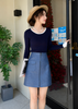 Woman in navy top and blue skirt exiting a building with plants and decorative items in the background.