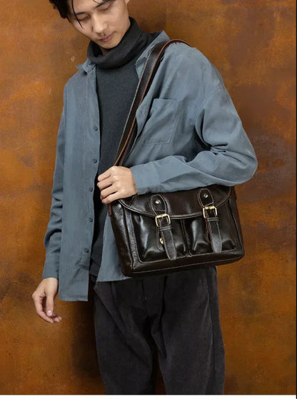 Brown leather messenger bag for men shown carried by hand with compact satchel shape and front buckle details.