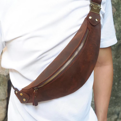 A classic leather messenger bag with a minimalist design, leaning against a brick wall outdoors.