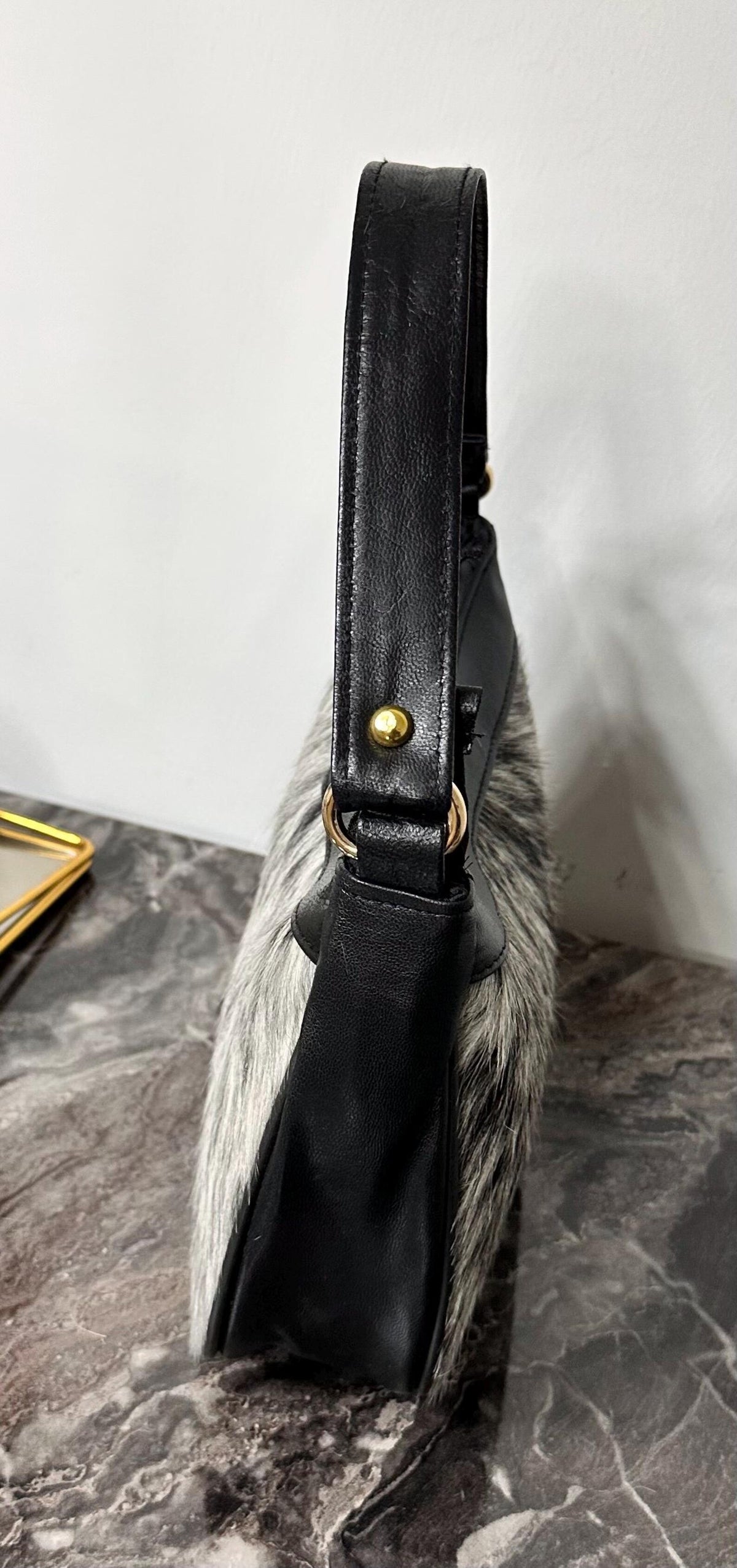 Cowhide bag styled as a shoulder handbag with soft gray hair-on hide, black accents, and curved silhouette.