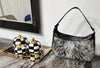 Cowhide bag with gray, white and black hair-on hide, black leather trim, curved shape, and shoulder strap.