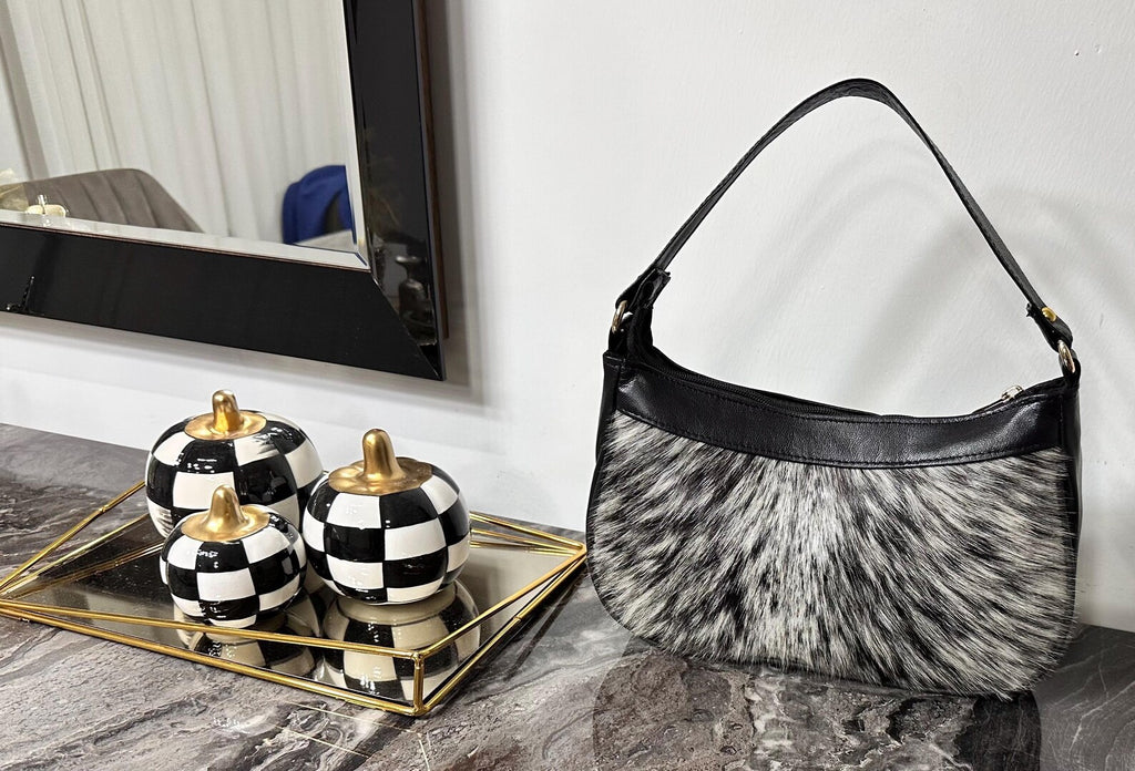 Cowhide bag with gray, white and black hair-on hide, black leather trim, curved shape, and shoulder strap.