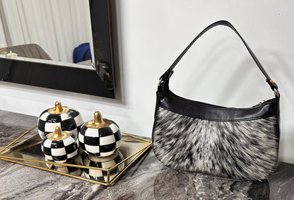 Cowhide bag with gray, white and black hair-on hide, black leather trim, curved shape, and shoulder strap.