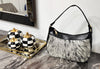 Cowhide bag with natural gray and black hide variation, zip-top opening, leather trim, and compact shoulder-carry shape.