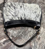 Cowhide bag with slim structured profile, black shoulder strap, gold-tone hardware, and natural hair-on cowhide patterning.