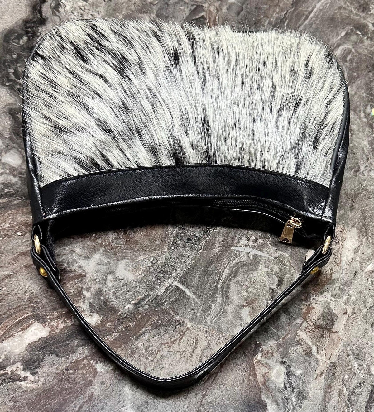 Cowhide bag with slim structured profile, black shoulder strap, gold-tone hardware, and natural hair-on cowhide patterning.