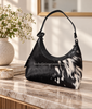 Cowhide purse with black and white hair-on hide, curved silhouette, black shoulder strap, and dark leather trim.