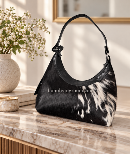 Cowhide purse with black and white hair-on hide, curved silhouette, black shoulder strap, and dark leather trim.