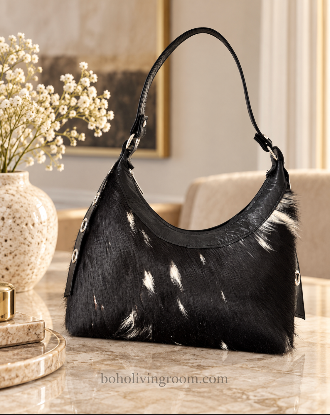 Cowhide purse with natural black-dominant hide pattern, soft white markings, curved body, and metal-tone strap hardware.