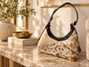 Cowhide shoulder bag with camel and white hair-on hide, black trim, curved shape, and dark shoulder strap.