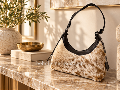 Cowhide shoulder bag with camel and white hair-on hide, black trim, curved shape, and dark shoulder strap.