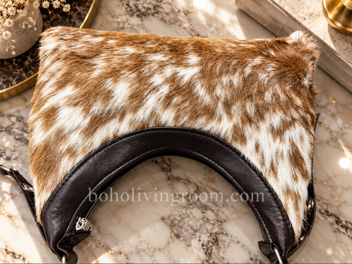 Cowhide shoulder bag with curved hobo-inspired silhouette, black shoulder strap, white markings, and warm camel-toned hide.