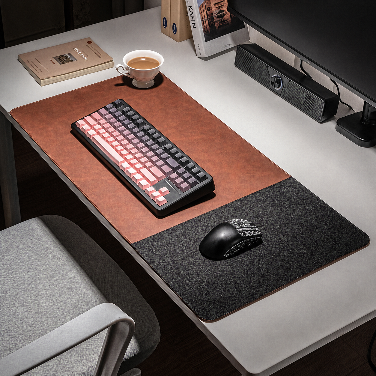 A large desk mat with a two-tone design, featuring a brown faux-leather top half and a dark gray felt bottom half, styled on a white desk with a keyboard, mouse, and a cup of coffee.