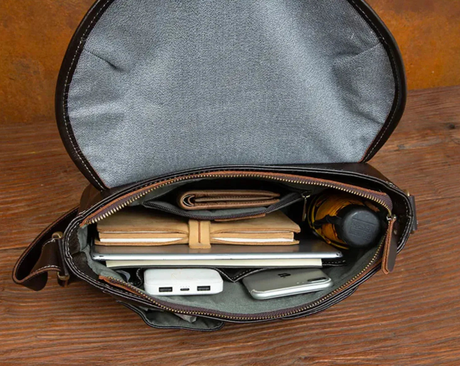 Mens brown leather messenger bag beside tablet showing compact proportions for electronics and everyday personal essentials.
