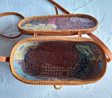 Artisan weaving an oval rattan crossbody bag in a lush forest setting.