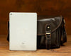 Small leather messenger bag shown from the back while worn crossbody with adjustable brown shoulder strap.