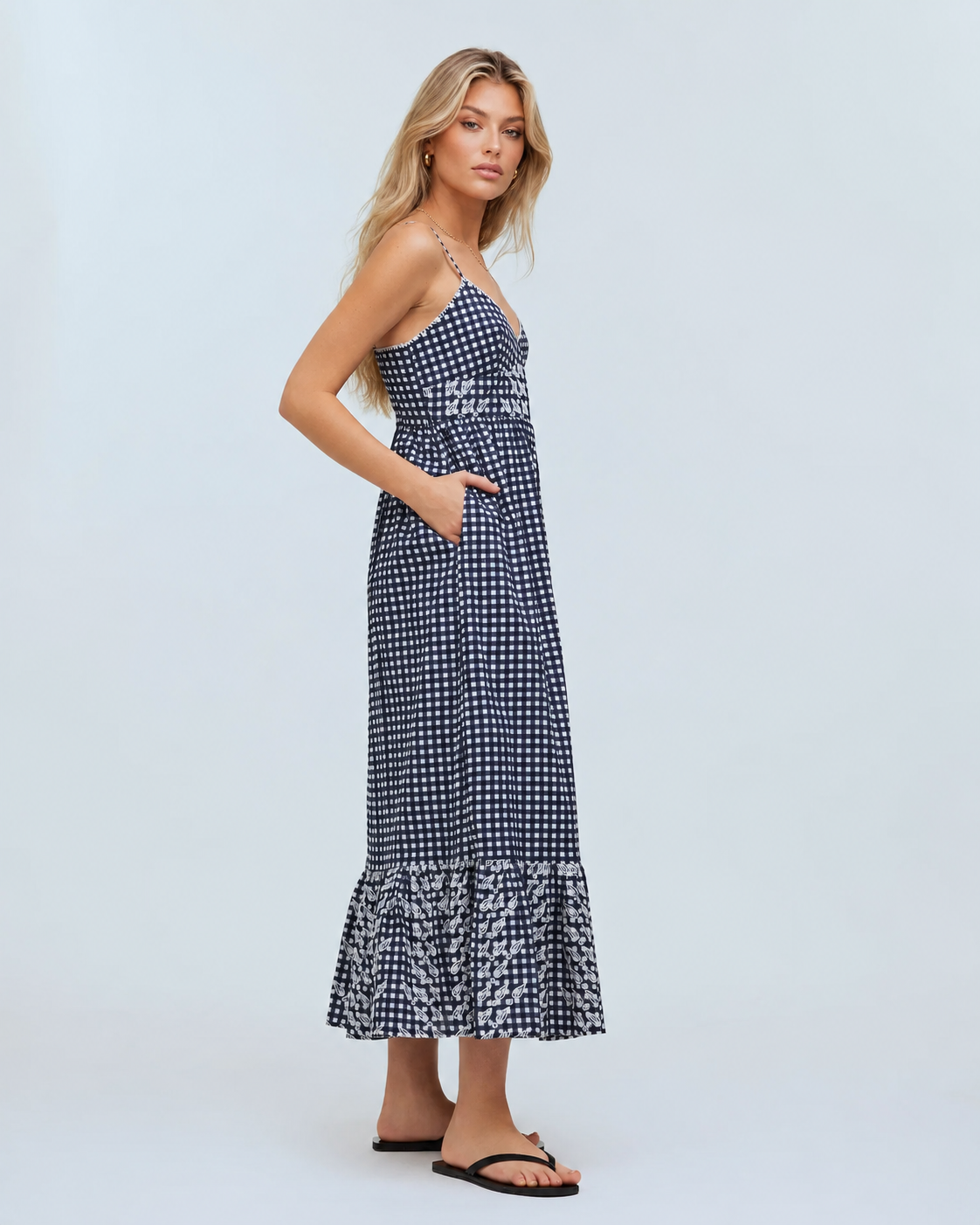 Summer gingham maxi dress featuring slim straps, a V-neck bodice, side pockets, and a ruffled lower hem.