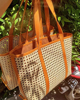 Artisanal rattan tote bag placed on a sandy beach backdrop, highlighting its suitability for beach outings with its durable material and stylish look