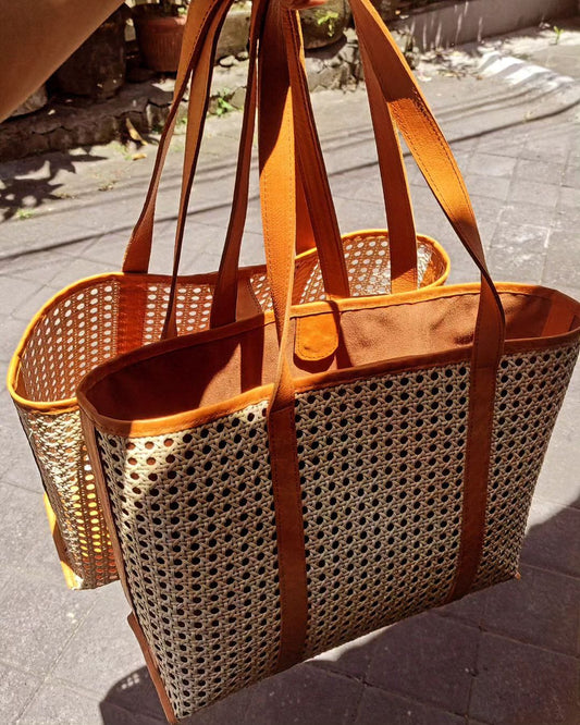 Close-up of a handwoven rattan tote bag with leather straps, showcasing the intricate weaving pattern and natural color variations.