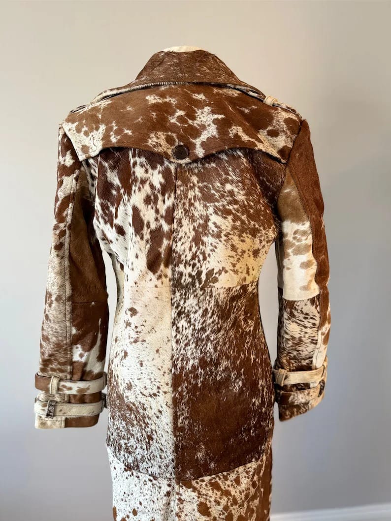 Country western women’s cow skin coat in black, brown, and white. Natural fur trench coat perfect for rodeo fashion and outdoor events.